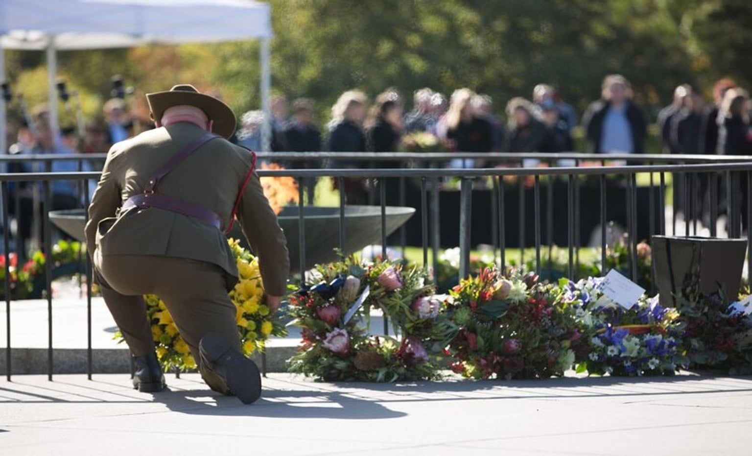 Person in military dress, laying a wreath at the eternal flame next to three other wreaths